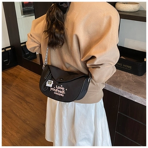 Model wearing black crescent shoulder bag with Love Yourself embroidery and chain strap