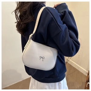 Detail view of white leather crescent shoulder bag with silver bow accent on model
