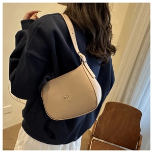 Detail of elegant beige hobo shoulder bag with a metal bow accent on a model