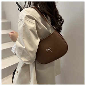 Brown leather baguette bag with silver bow detail shown on a model's shoulder