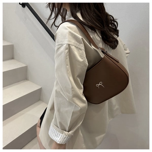 Close-up of a brown leather half-moon underarm bag with a silver bow buckle on a model