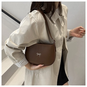 Detail of a brown leather saddle bag featuring a delicate white bow metal ornament
