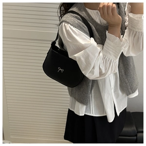 Close-up of minimalist black underarm bag with silver bow accent on model's shoulder