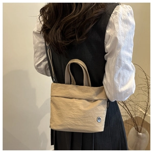 Close-up of beige nylon bucket bag featuring a round metal M logo and side fabric label