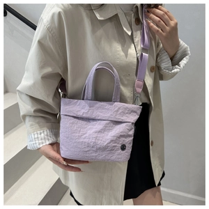 Close-up of lavender bucket bag with dual handles and wide woven shoulder strap on model