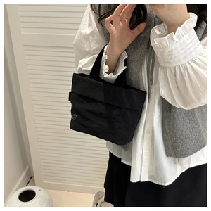 Detalle del bolso tote de nailon negro con logo metálico llevado por una modelo con ropa casual