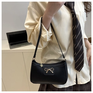 Detail of black pebbled leather baguette bag with golden bow and flower zipper pull