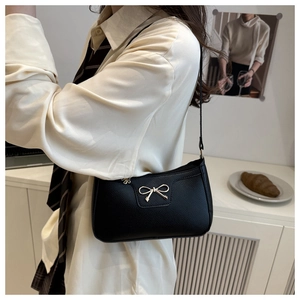 Close-up of black baguette bag with gold metal bow detail and pebbled texture