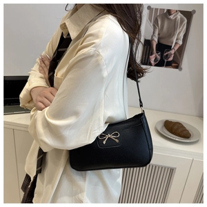 Close-up of elegant golden bow hardware on a black pebbled leather underarm shoulder bag