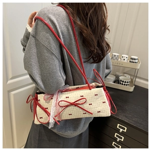 Detail of sweet bow baguette bag showing red ribbon accents and lace trim on cream canvas