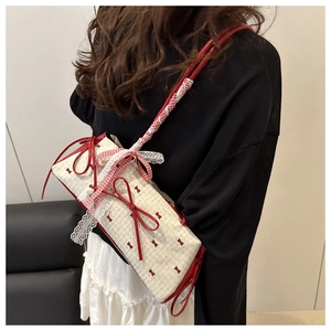 Close-up of red bow prints and white lace detailing on a cream canvas shoulder bag