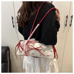 Close-up of canvas underarm bag with red bow patterns, lace detail, and leather strap