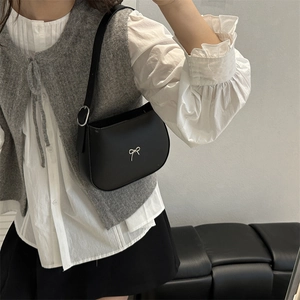 Elegant black matte shoulder bag with silver metal bow worn by model in casual style