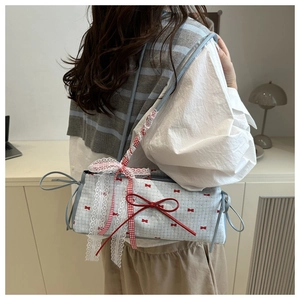 Detail of blue canvas shoulder bag featuring red bows, lace trim, and plaid straps