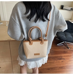Detail der beige gewebten Tragetasche mit braunen Ledergriffen und verstellbarem Riemen