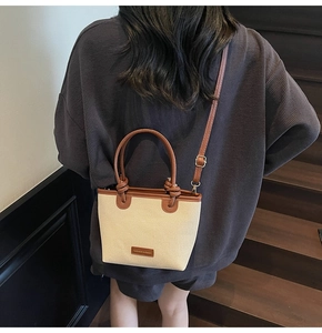 Detailed shot of canvas bucket bag with brown leather trim on a dark wooden staircase