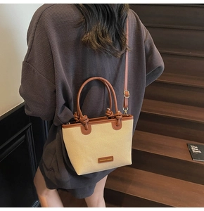 Close-up of woven straw bucket bag with brown leather handles and adjustable shoulder strap