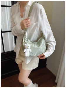 Detail view of light green pleated shoulder bag with white teddy bear charm on model