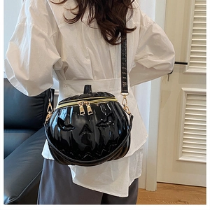 Detail of black glossy pumpkin-shaped crossbody bag with gold zippers and face design