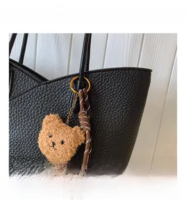 Detail of black lychee leather tote bag featuring a plush brown bear and woven rope charm