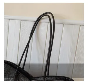 Detailed close-up of textured lychee grain leather and sleek dual shoulder straps on a black tote bag