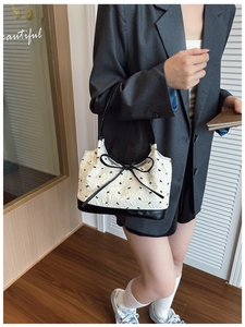 Detail of white textured fabric bag featuring black bow embroidery and leather strap
