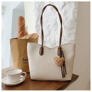 Detail of off-white lychee pattern tote bag with wavy rim and plush bear charm