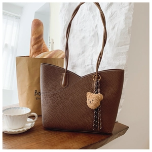 Close-up of brown pebble leather tote bag with V-shaped stitching and bear charm accessory
