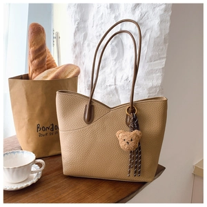 Detailed view of lychee texture faux leather tote bag with a plush bear charm on a wooden table