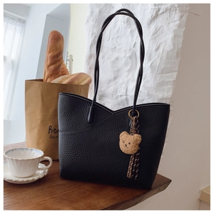 Close-up of black litchi grain leather tote bag with V-shaped stitching and bear charm