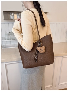 Detail of a dark brown pebble leather tote bag with a plush bear and tassel charm