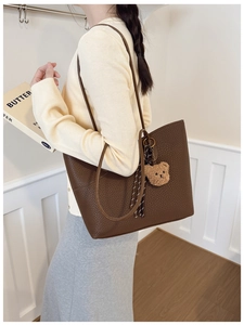 Detail of dark brown leather tote bag with plush bear charm worn over the shoulder