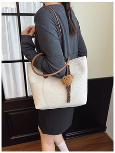Close-up of white pebble leather tote bag with brown handles and cute bear charm
