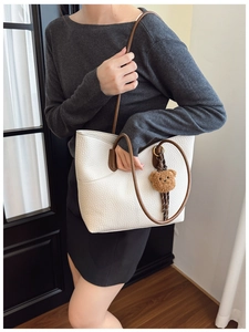 Close-up of white pebble leather tote bag featuring a brown teddy bear charm and handle