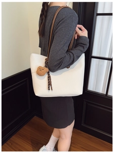 Detail of white pebbled leather tote bag with brown straps and cute bear charm