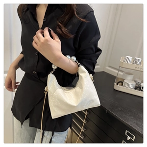 Detail of white pearlescent handbag with large pearl handle and slim metal chain strap