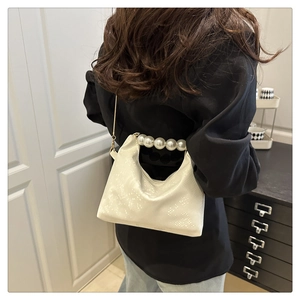Detail of elegant off-white handbag with pearl handle and gold chain strap