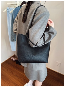 Close-up of black lychee texture leather tote bag worn with a grey business suit