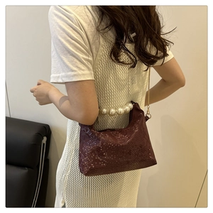 Detail of burgundy faux snakeskin handbag with elegant pearl handle and gold chain