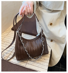 Detail of dark brown woven leather texture with chunky silver chain on a crossbody bag