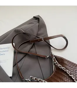Detail of dark brown woven leather bag featuring adjustable strap and silver metal chain