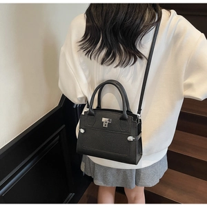 Detail of black litchi leather handbag with silver twist lock shown on model
