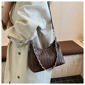 Detail of dark brown woven crescent bag with silver chain strap on model shoulder