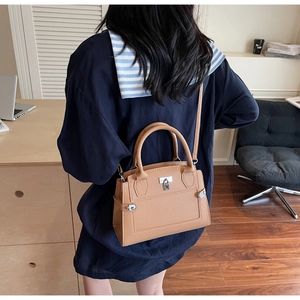 Macro view of a brown trapezoid leather handbag featuring a silver lock and dual top handles