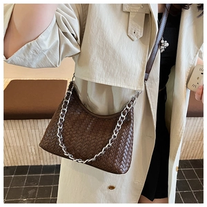 Detailed shot of dark brown woven hobo bag with silver chain on beige trench coat