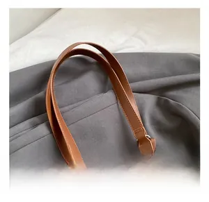 Close-up of brown leather woven tote bag detail showing comfort handle and metal hardware