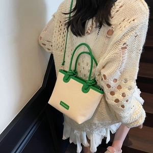 Women's woven bucket bag with green PU handles shown in a lifestyle street setting