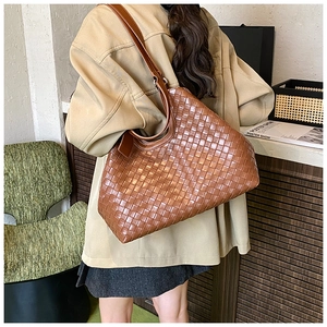 Brown woven leather tote bag shown on shoulder in a stylish lifestyle interior setting
