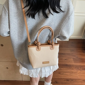 Minimalist beige woven canvas bucket bag with brown leather handles and a long shoulder strap