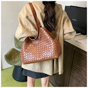 Detailed view of brown woven leather tote bag texture and shoulder strap fit on a model
